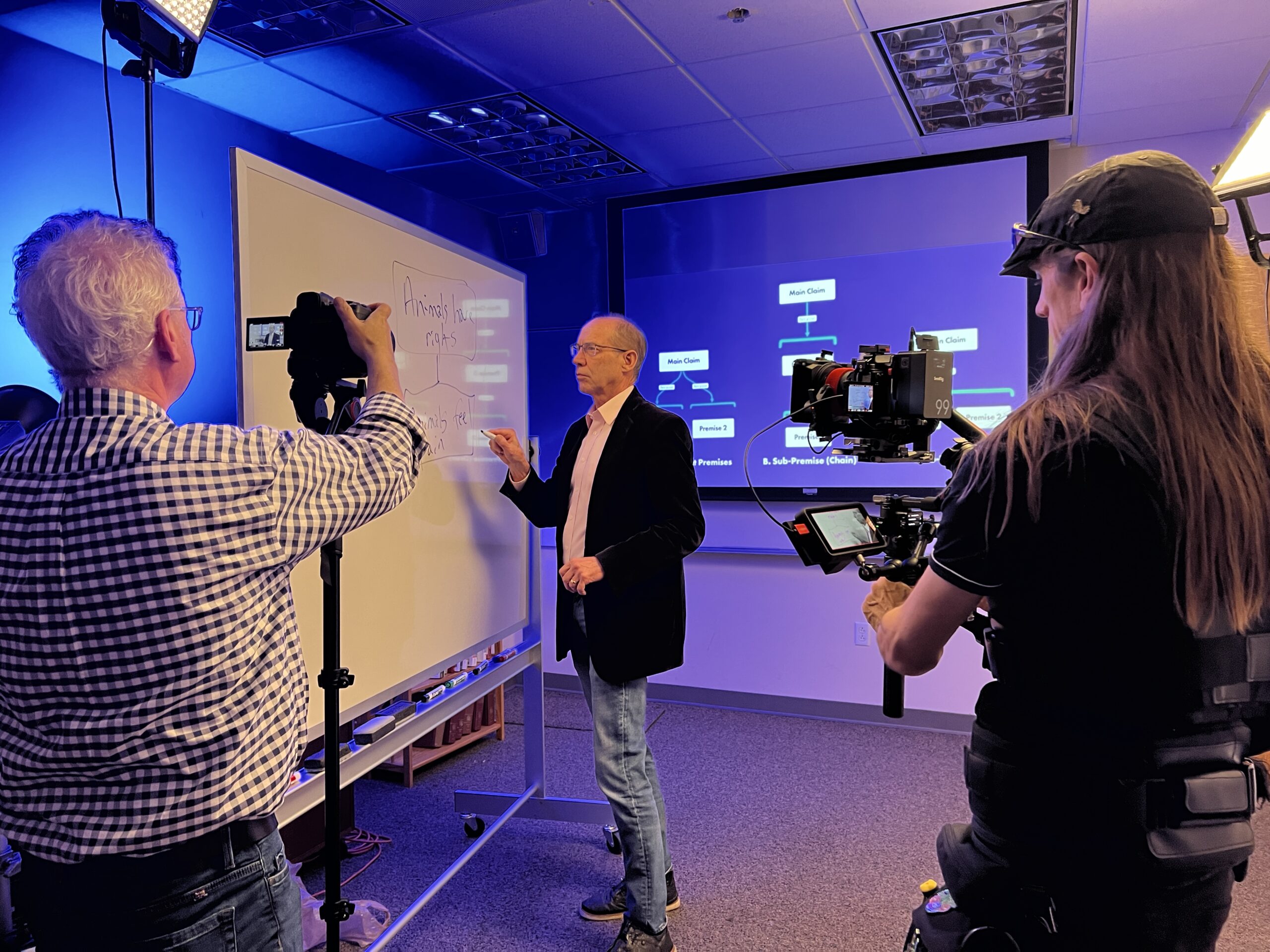 Gary Comstock writes on a dry erase board in front of cameras.